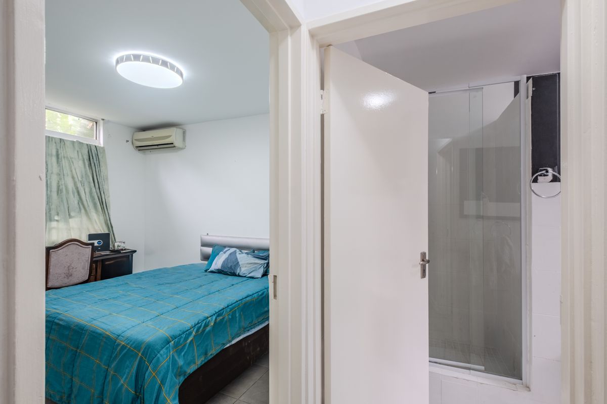 A bedroom featuring a split-system air conditioner and an adjacent en-suite bathroom with a glass-enclosed shower.