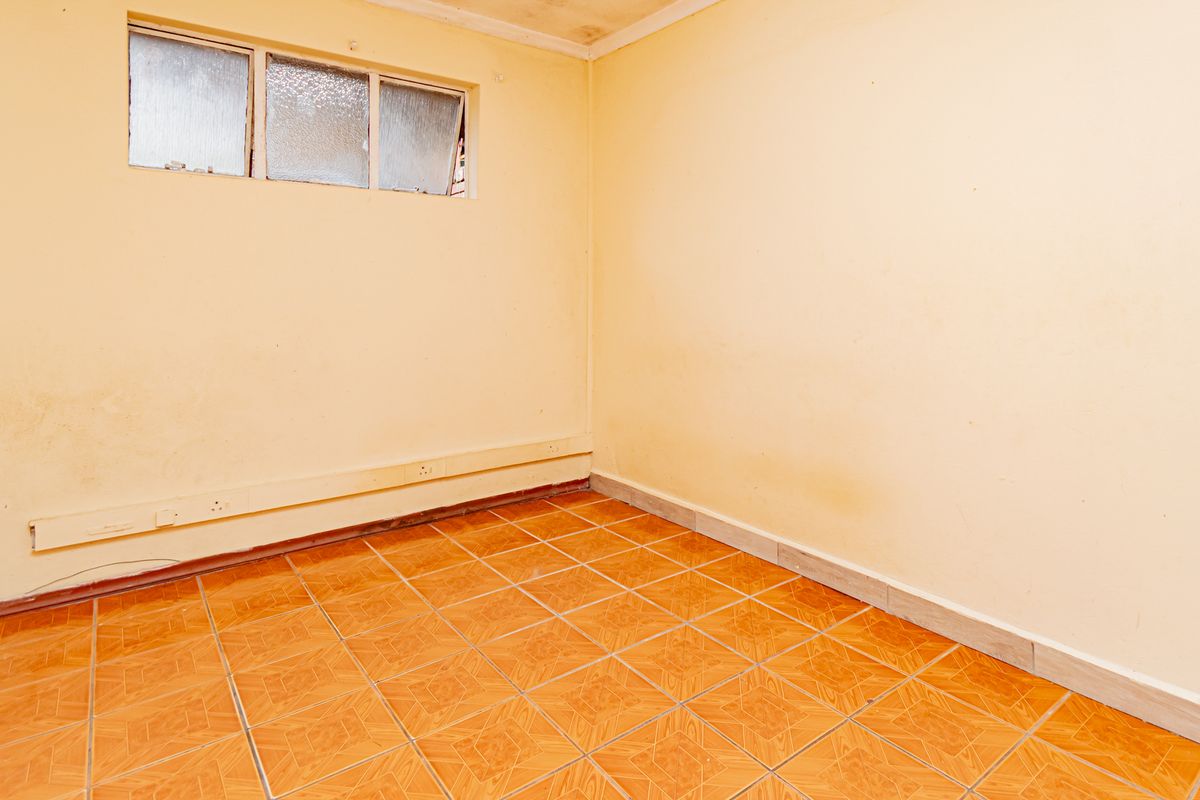An empty bedroom featuring tiled flooring and a high-level window, requiring cosmetic updates to the walls and ceiling.