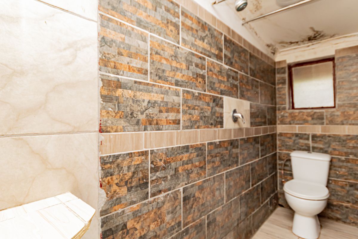 A bathroom featuring tiled walls and floor, a toilet, and a shower head, currently showing signs of ceiling water damage and unfinished tiling.