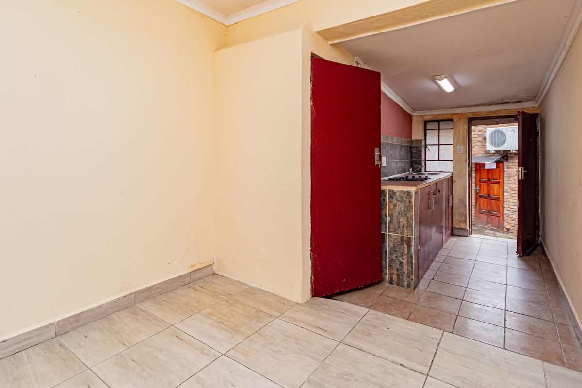 A compact, empty kitchen area featuring tiled flooring, built-in cabinetry with a hob, and direct access to an exterior space.