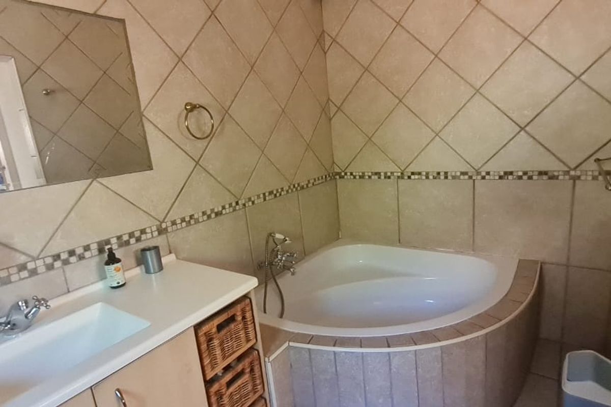A functional bathroom featuring a corner bathtub, vanity cabinet with integrated basin, and neutral wall tiling.