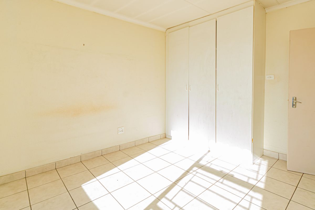 An empty bedroom featuring tiled flooring and built-in white wardrobes, offering a blank canvas for potential updates and personalization.