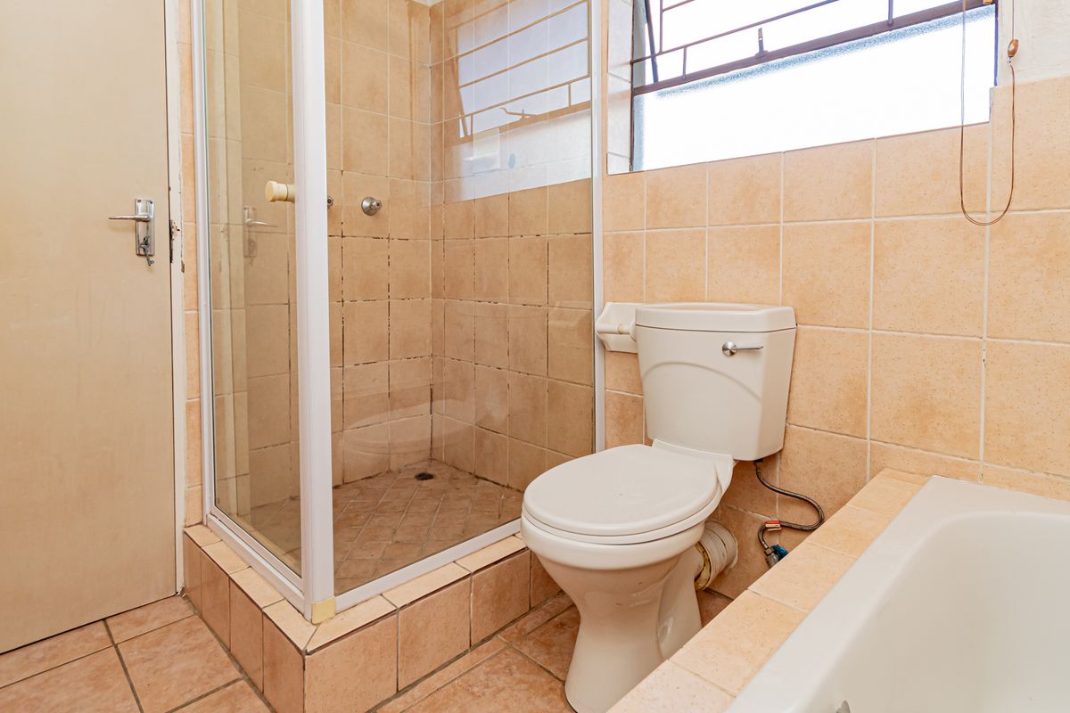 A dated bathroom featuring a shower cubicle, a standard toilet, and a bathtub with beige wall and floor tiling.