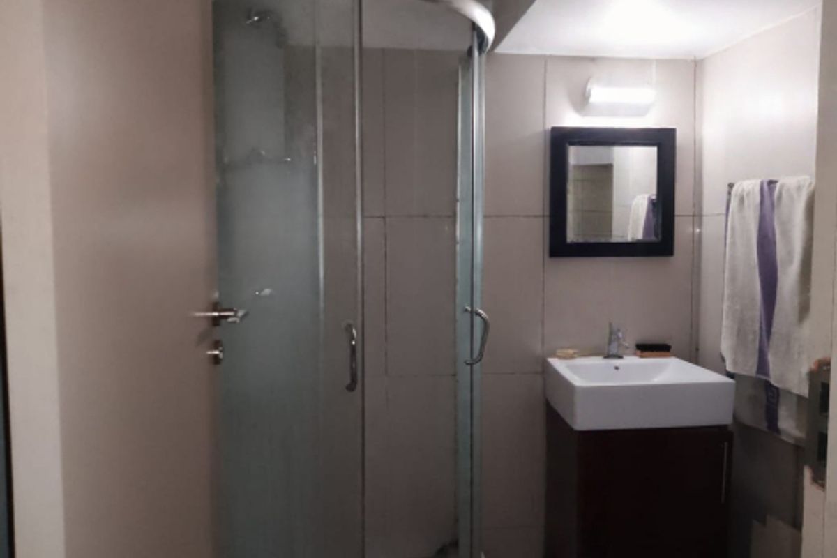 Compact bathroom featuring a corner glass shower enclosure, modern square basin with vanity cabinet, and wall-mounted mirror.