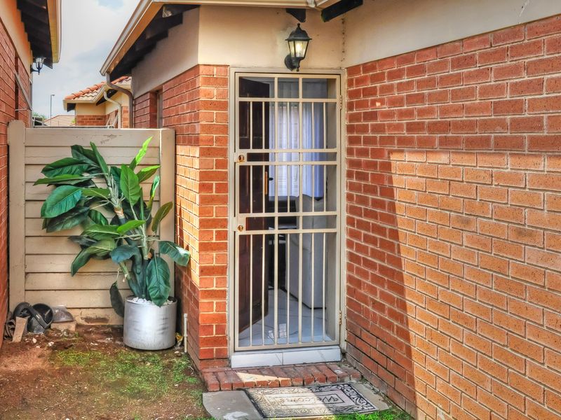 A rear exterior view of the townhouse featuring a brick facade, a secure metal gate, and an exterior wall light.