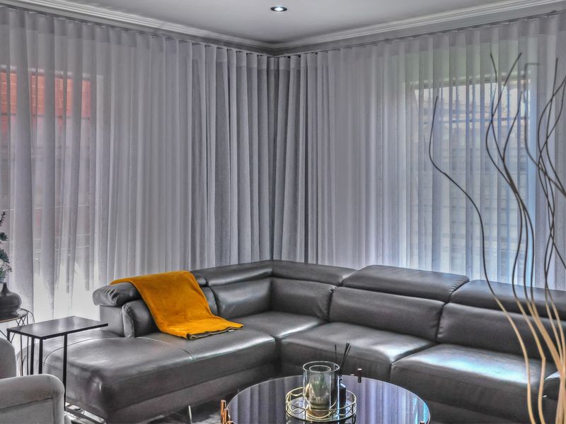 A well-lit living room featuring modern recessed downlights, decorative cornice detailing, and floor-to-ceiling sheer curtains providing soft natural light.