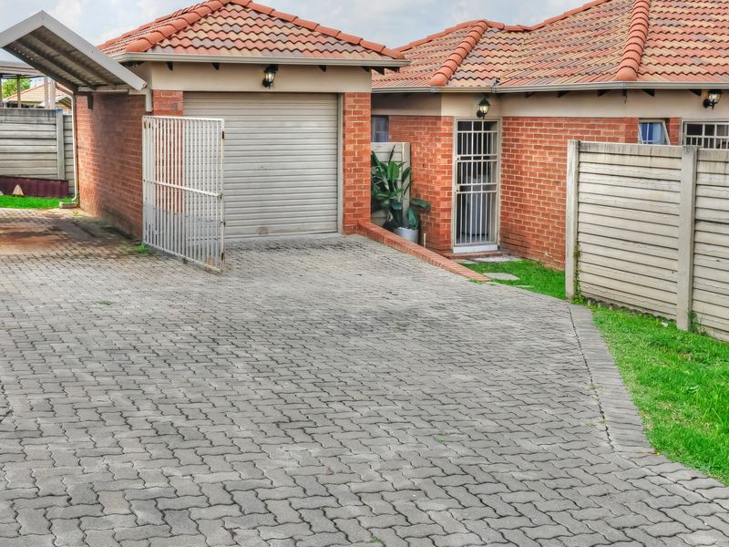 Front exterior view of a townhouse featuring a brick facade, tiled roof, paved driveway, single garage, and secure gated entrance.