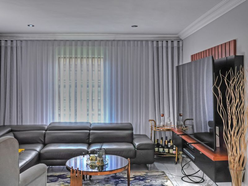A well-maintained living room featuring tiled flooring, recessed downlighting, crown molding, and a built-in media console.