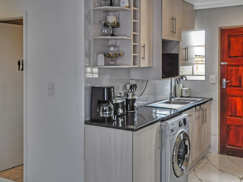 Compact kitchen featuring modern light-wood cabinetry, granite countertops, tiled backsplash, and an integrated washing machine, providing a functional and efficient workspace.