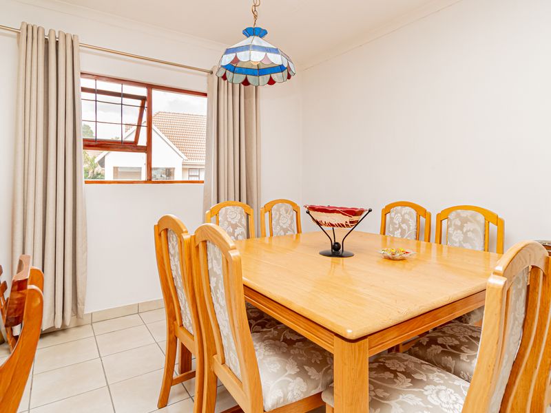 A bright dining room featuring neutral tiled flooring, coved cornicing, and a timber-framed window, providing a functional space for family meals.