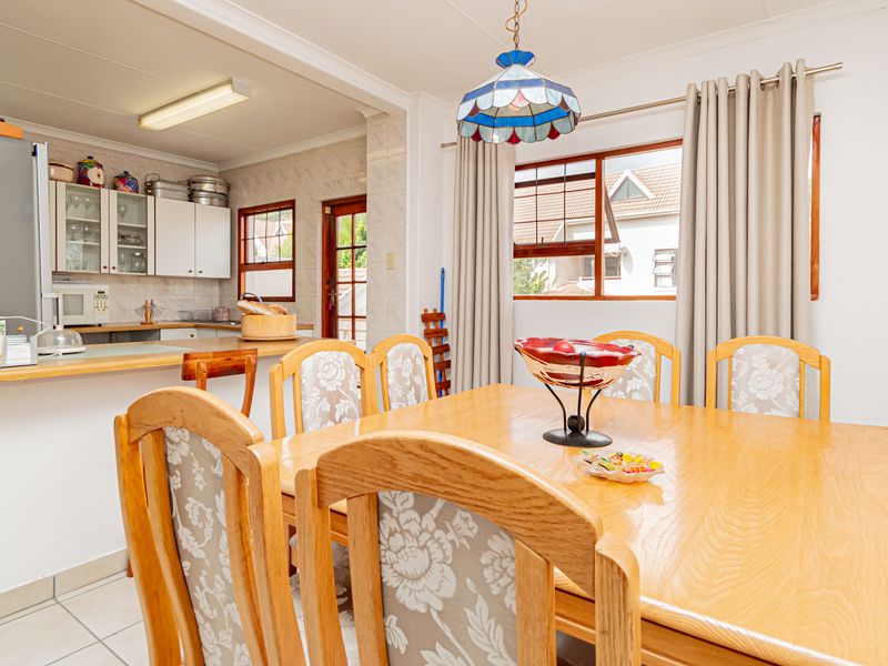 Open-plan dining area and kitchen featuring tiled flooring, timber window frames, and a breakfast bar, offering a functional layout for daily living.