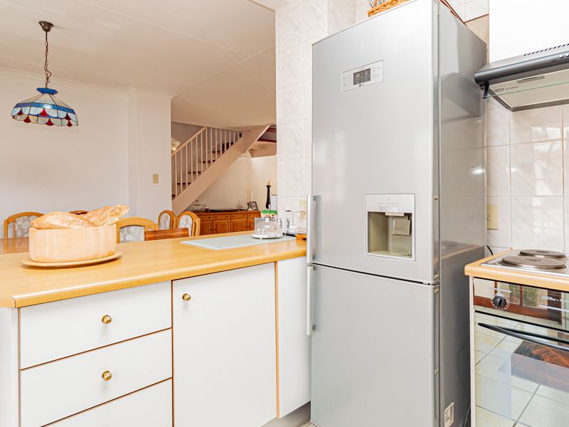 Open plan kitchen and dining area featuring white cabinetry, laminate countertops, built-in stove, and tiled flooring with a view towards the staircase.