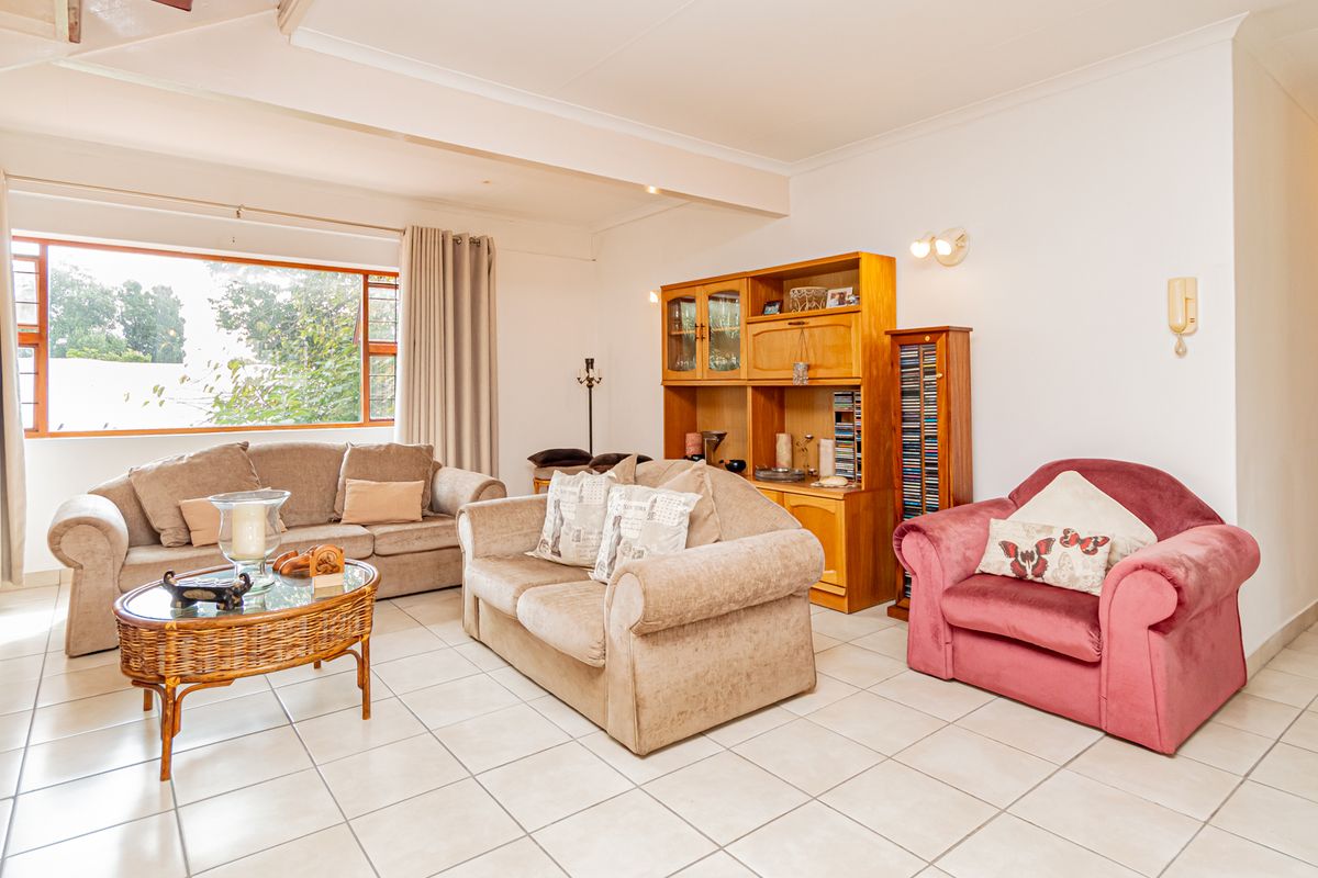 A spacious living room featuring neutral tiled flooring, a large window providing natural light, and a coved ceiling.