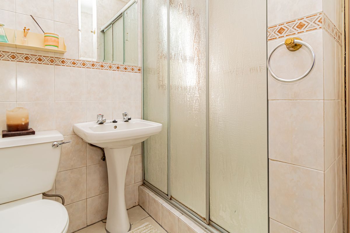 A functional bathroom featuring a pedestal washbasin, toilet, and a glass-enclosed shower with neutral wall tiling.