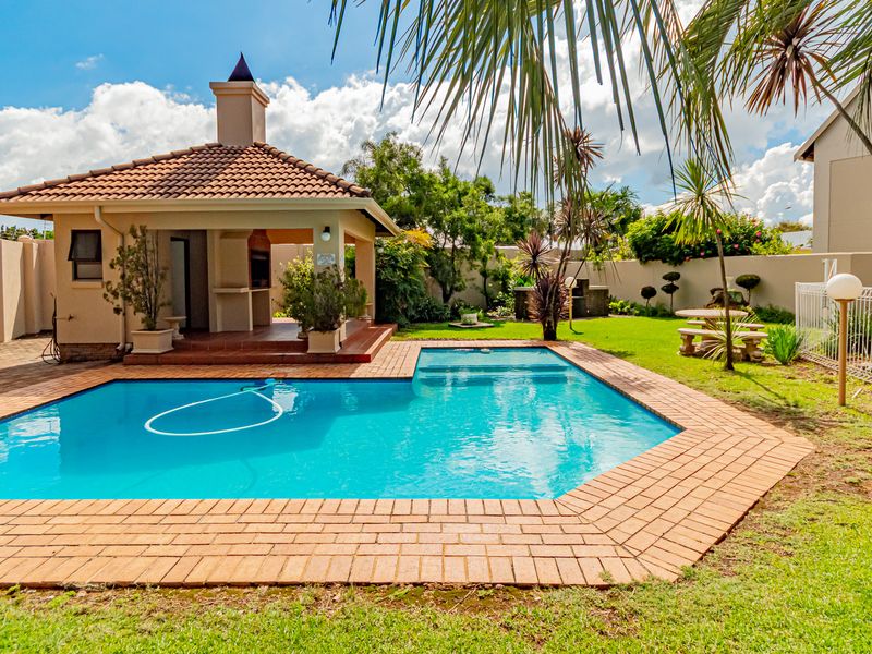 Outdoor entertainment area featuring a swimming pool with brick coping and a covered patio with a built-in braai and chimney.