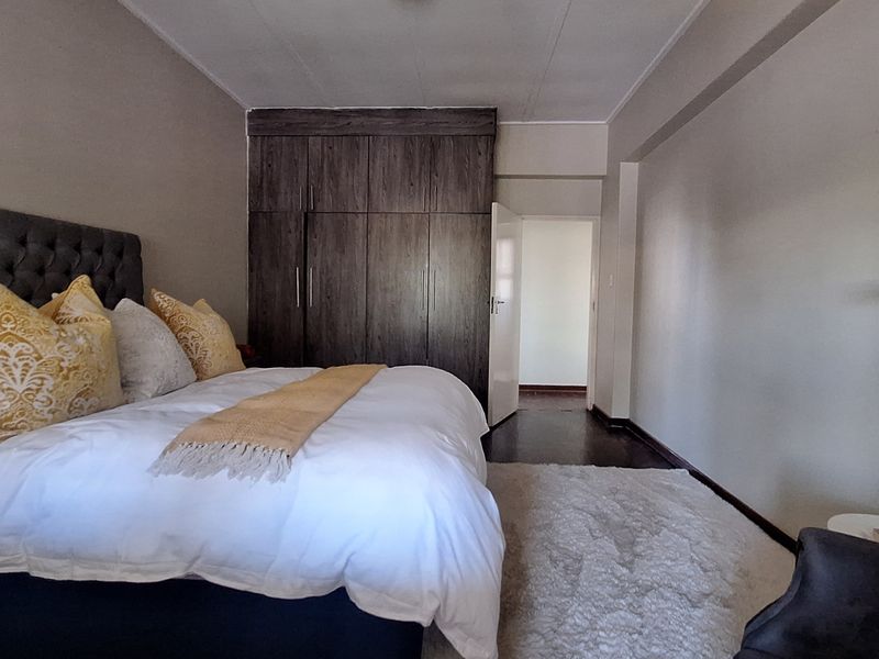 A well-maintained bedroom featuring dark wood-finish built-in cupboards and neutral wall tones, providing a clean and functional living space.
