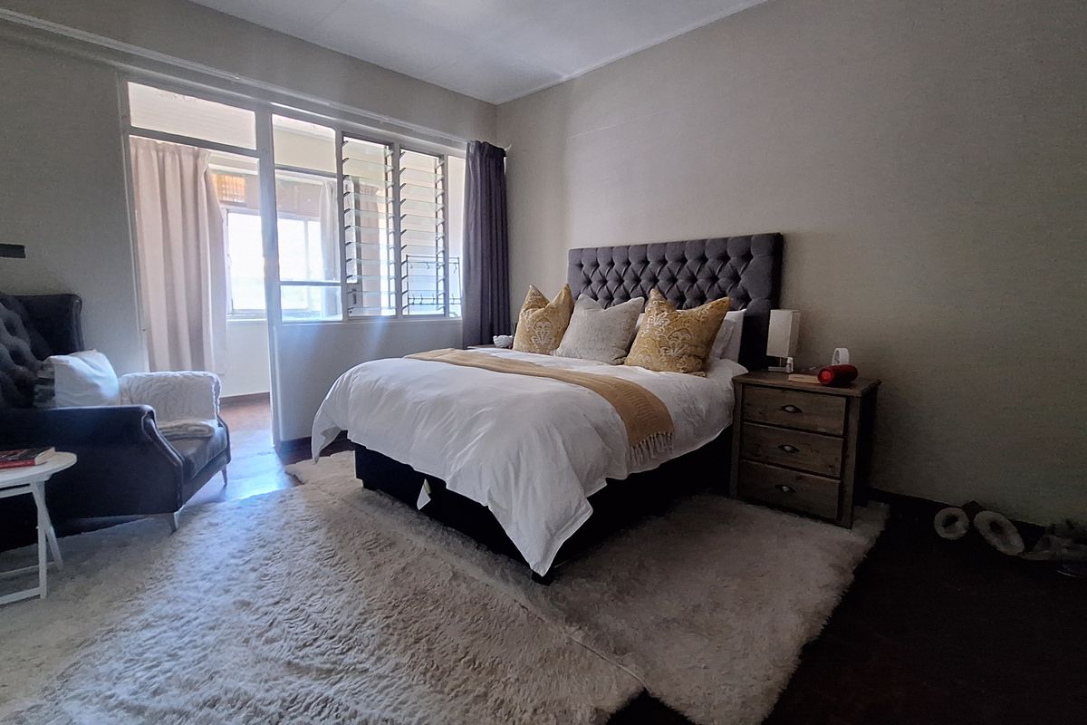 A well-lit bedroom featuring parquet flooring and a large glass sliding door leading to an enclosed balcony area.
