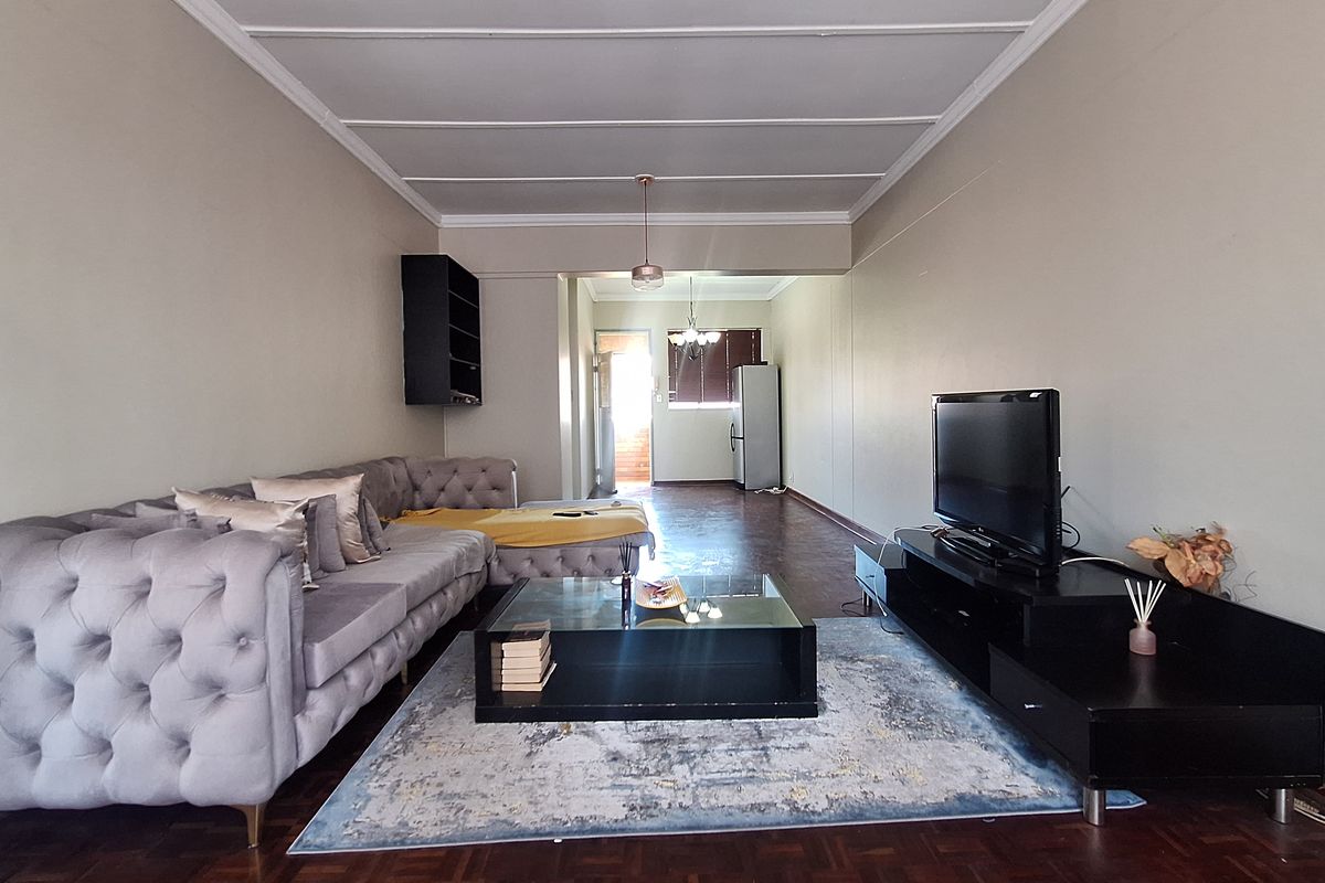 Spacious living room featuring classic parquet flooring, decorative ceiling panelling, and neutral wall tones, offering a comfortable and versatile living space.