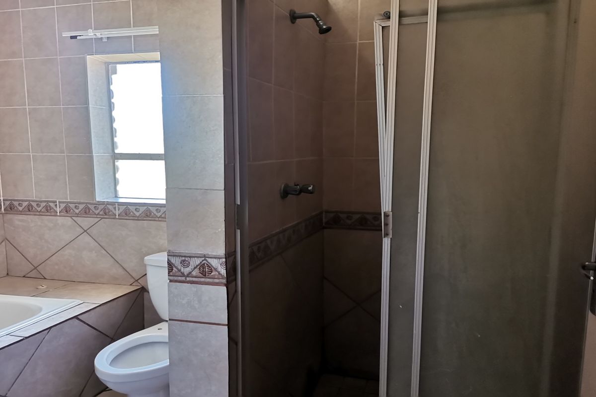 A dated bathroom featuring a built-in bathtub, toilet, and a shower enclosure with a damaged door frame requiring repair.