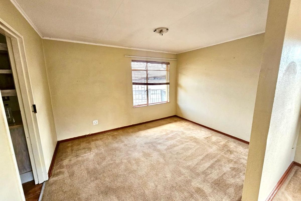 A vacant bedroom featuring neutral wall tones, carpeted flooring, and a window with fitted blinds, offering a blank canvas for personalization.
