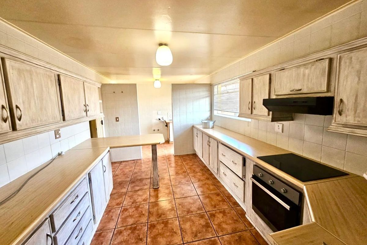 A functional kitchen featuring extensive cabinetry, built-in oven, electric hob, extractor fan, and tiled flooring, offering a practical layout for culinary activities.