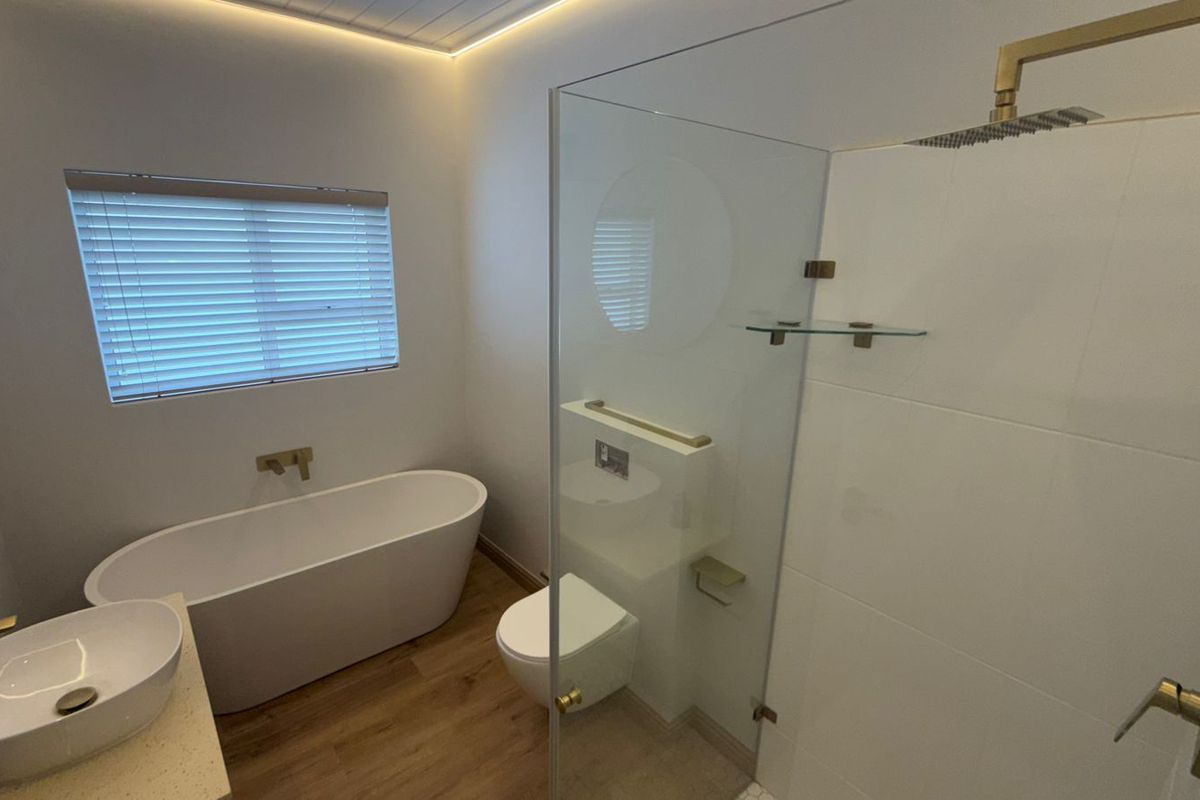 Modern bathroom featuring a freestanding bathtub, walk-in shower with rain head, wall-hung toilet, and elegant brass fixtures with timber-look flooring.