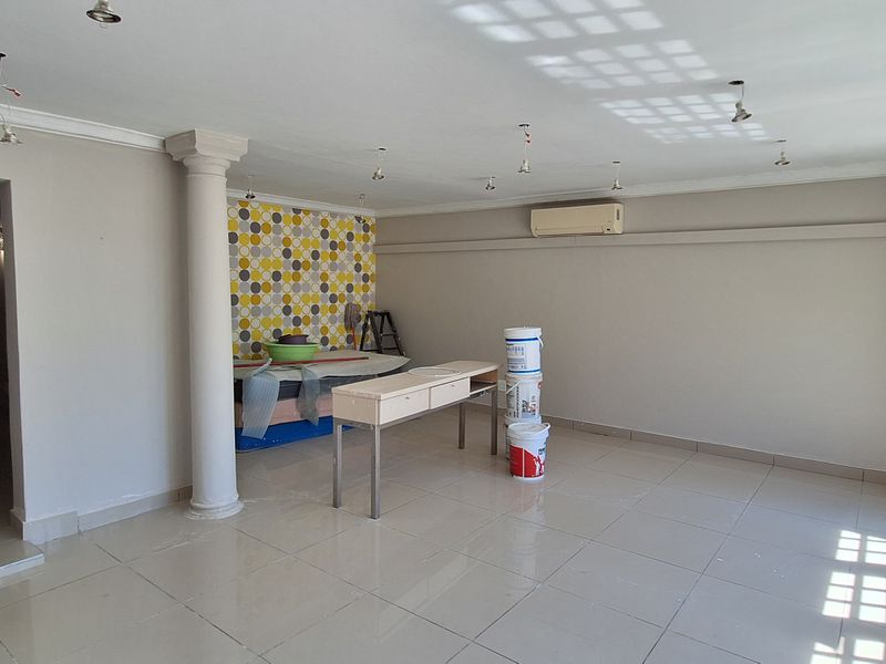 Spacious open-plan living area featuring tiled floors, a decorative column, wall-mounted air conditioning, and large wooden-framed glass doors leading to the exterior.