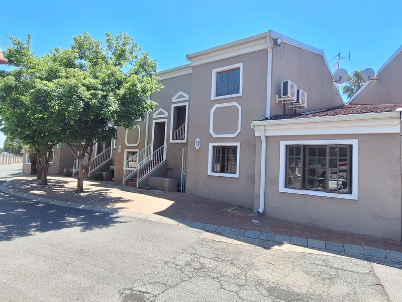 Front exterior view of a townhouse complex featuring a stucco facade, paved driveway, and external air conditioning units under a clear blue sky.