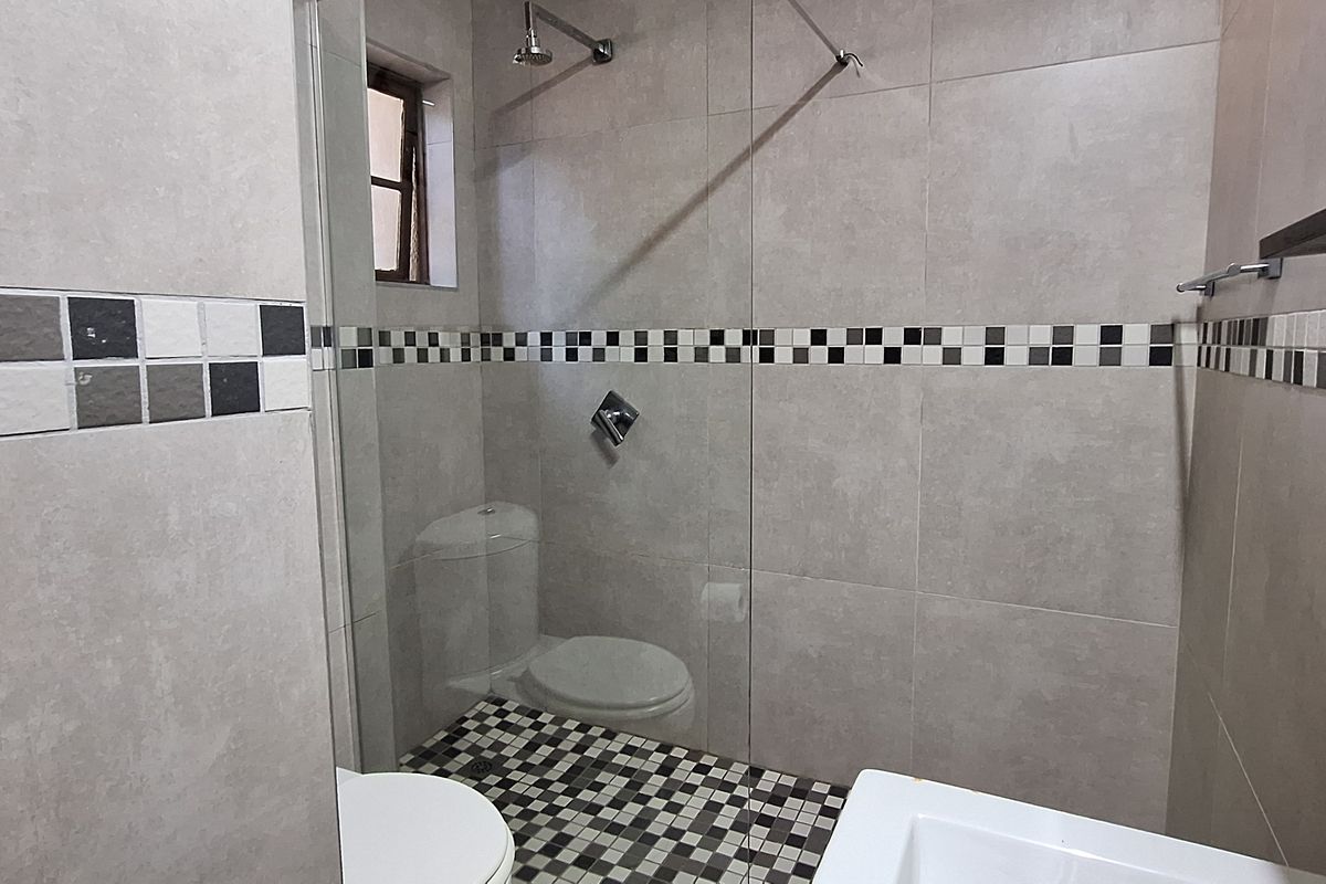 A clean, modern bathroom featuring a glass-enclosed shower, neutral wall tiling with a decorative mosaic border, and a functional toilet.