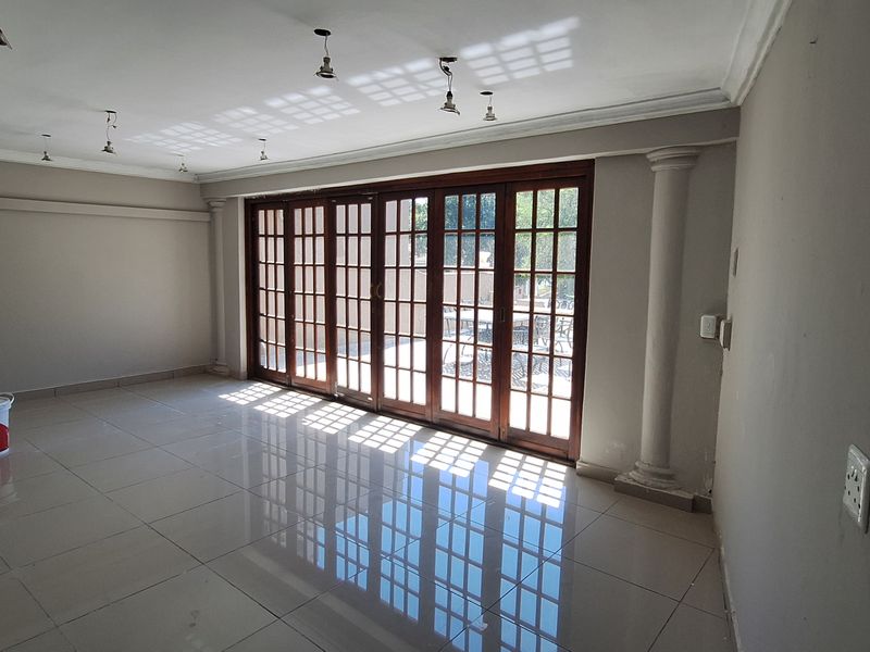 Spacious living area featuring polished tile floors, decorative columns, and large wooden folding doors that provide ample natural light and access to the outdoors.
