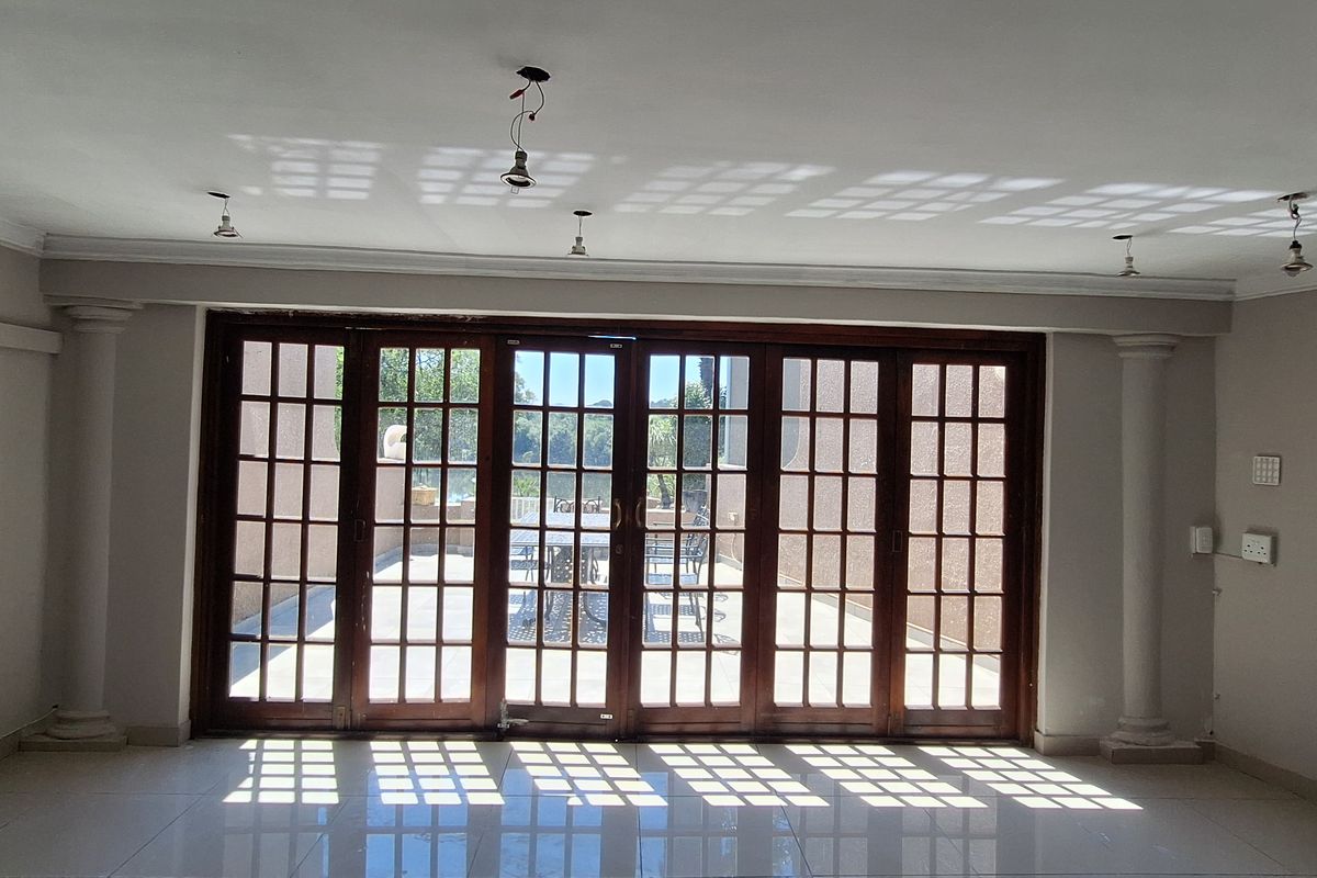 Spacious living area featuring large wooden framed french doors, decorative columns, and neutral tiled flooring, offering abundant natural light and access to the patio.