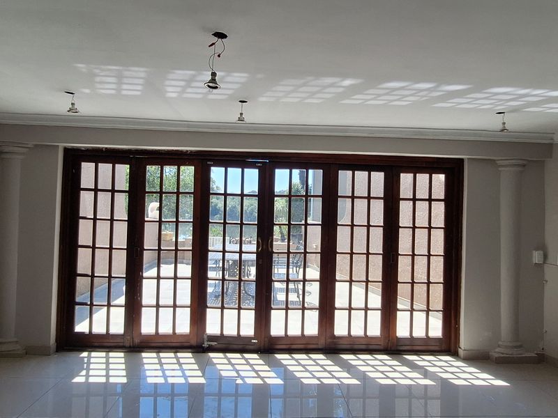 Spacious living area featuring large wooden framed french doors, decorative columns, and neutral tiled flooring, offering abundant natural light and access to the patio.