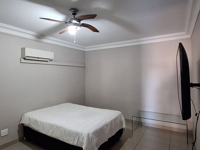A bedroom featuring tiled flooring, crown molding, a ceiling fan, and a wall-mounted split-system air conditioner.