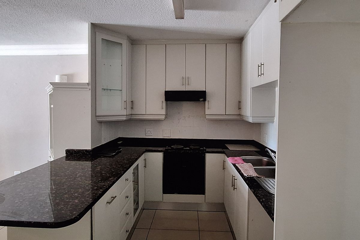 A functional kitchen featuring granite countertops, built-in cabinetry, an electric hob with extractor fan, and a double bowl sink.