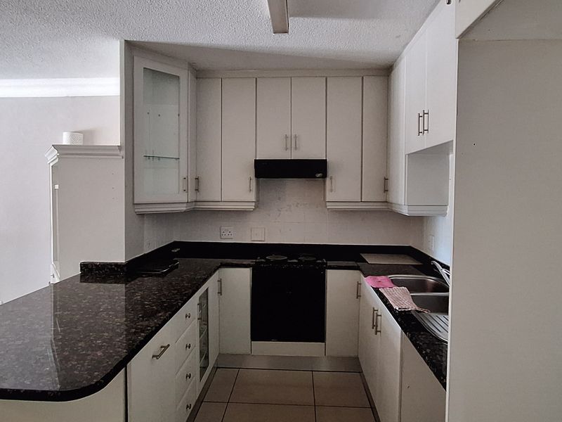 A functional kitchen featuring granite countertops, built-in cabinetry, an electric hob with extractor fan, and a double bowl sink.