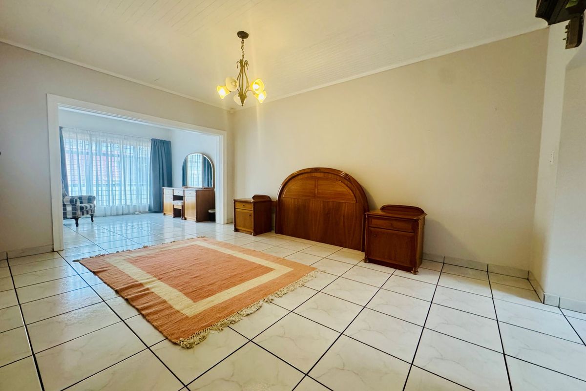Spacious bedroom featuring tiled flooring, a classic chandelier, and an adjoining sunroom area with large windows providing natural light.