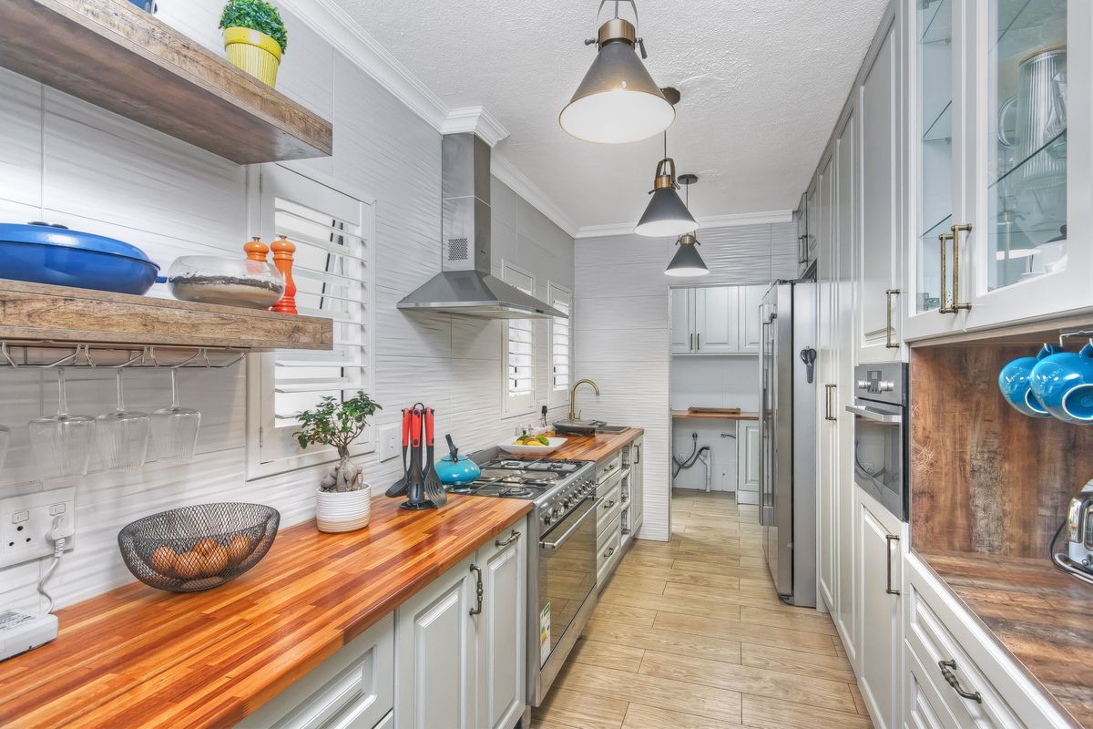 Modern galley-style kitchen featuring timber countertops, stainless steel gas range with extractor hood, and ample cabinetry, leading into a functional scullery area.