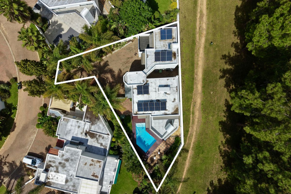 Aerial view of the property highlighting the roof structure, solar panel installation, swimming pool, and surrounding landscaped garden area.