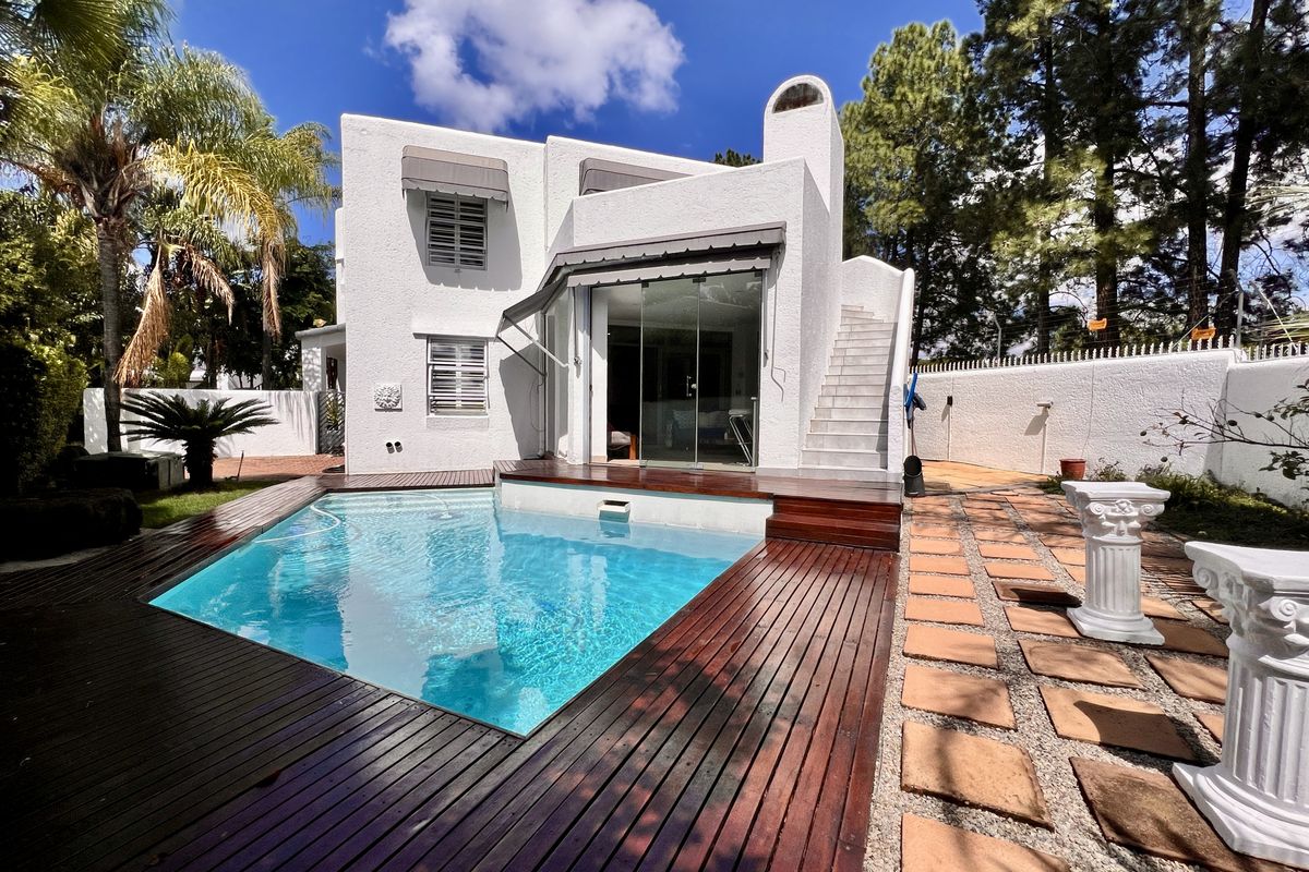 A well-maintained rear exterior featuring a swimming pool with timber decking, a white stucco facade, and an external staircase leading to the upper level.