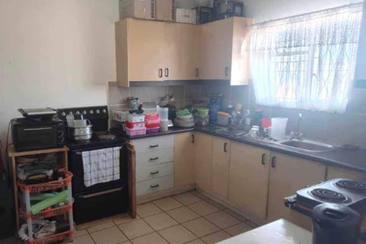A functional kitchen featuring laminate cabinetry, tiled flooring, a stainless steel sink, and a tiled backsplash, offering potential for modernization.
