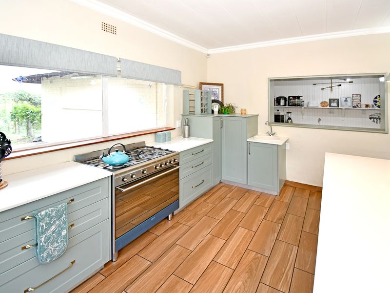 A well-maintained kitchen featuring light green cabinetry, a gas stove with oven, wood-look tile flooring, and a convenient pass-through window to the adjacent room.