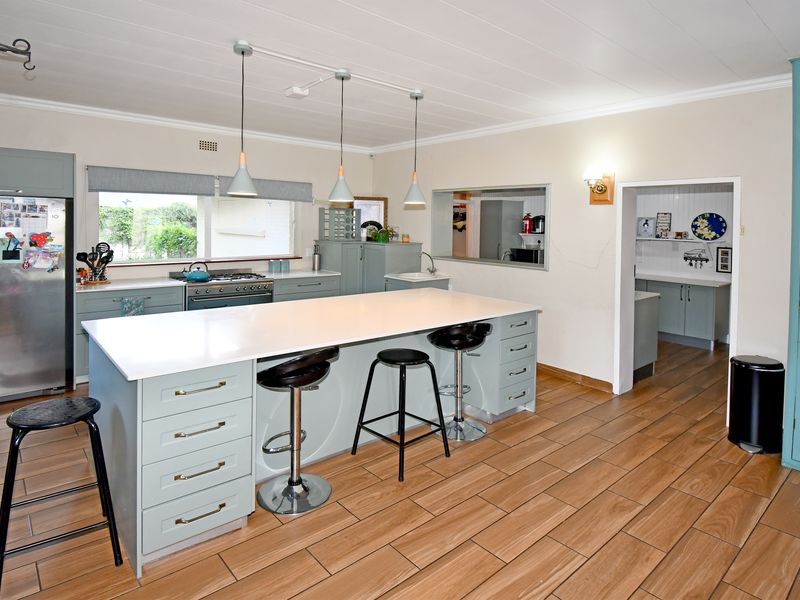 Spacious kitchen featuring a large central island, ample cabinetry, gas cooktop, and an adjoining scullery area with wood-look tiled flooring.