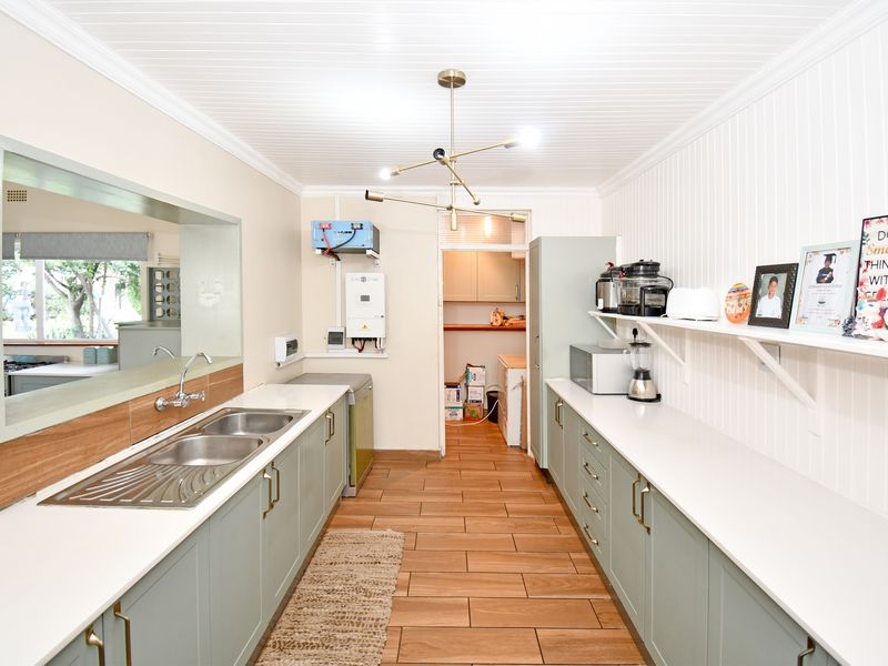 A well-maintained scullery featuring sage green cabinetry, stone countertops, a double stainless steel sink, and integrated inverter system with durable tiled flooring.