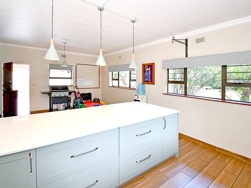 A bright kitchen featuring a large central island with quartz countertops, modern pendant lighting, and timber-look floor tiles.