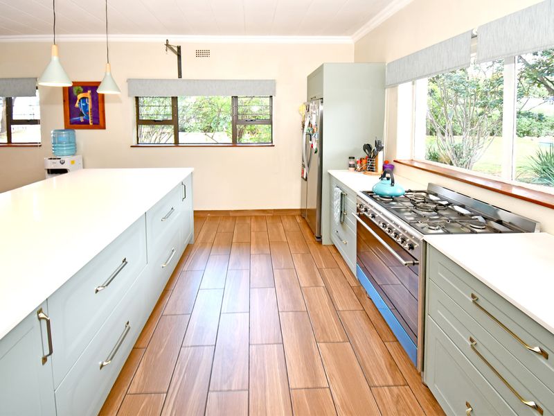A bright, modern kitchen featuring a large central island, gas stove, oven, and ample cabinetry with light-toned finishes and wood-look tiled flooring.