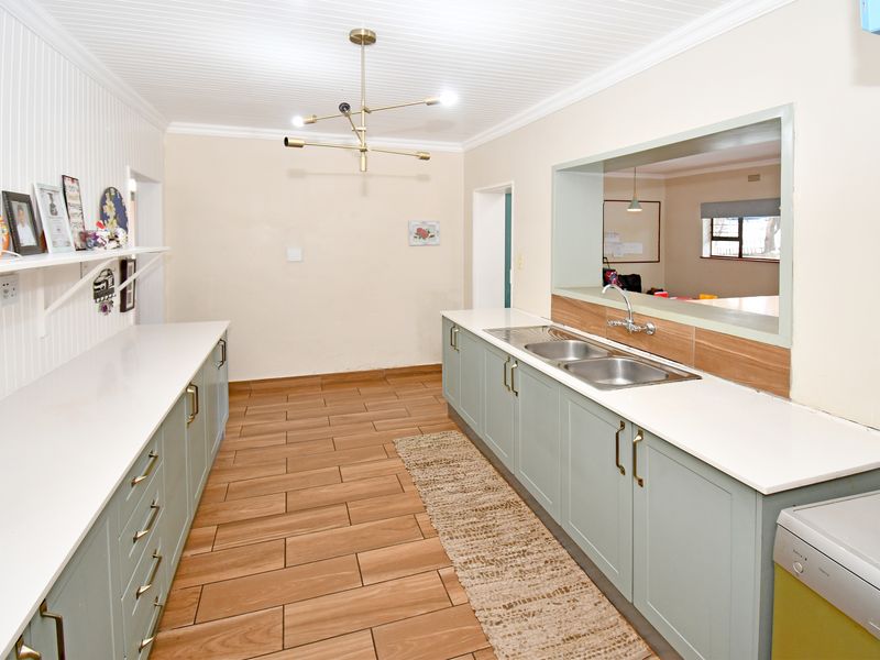 A well-maintained scullery featuring shaker-style cabinetry, quartz countertops, a double stainless steel sink, and modern lighting, providing ample prep and storage space.