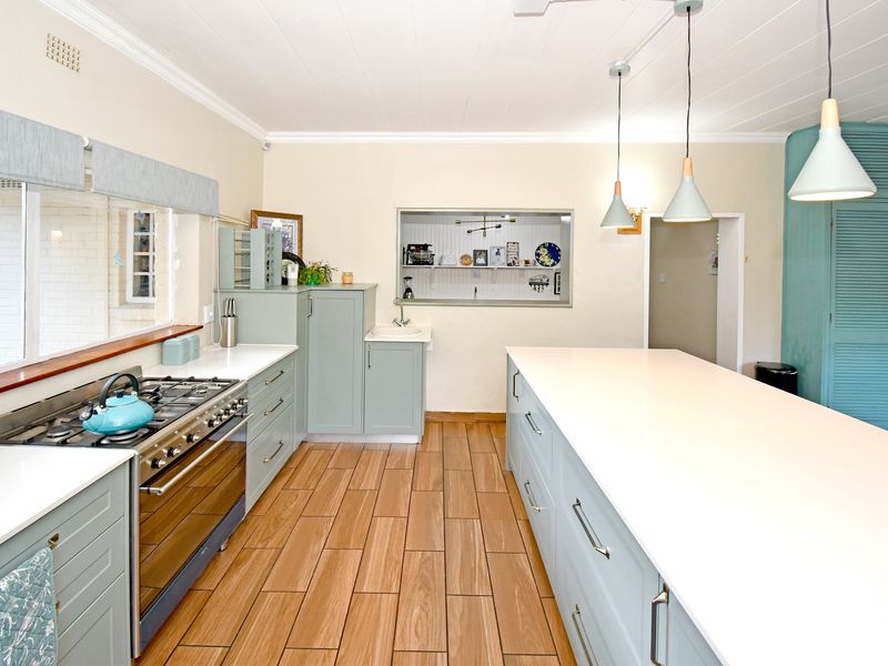 Modern kitchen featuring a large central island, gas stove, shaker-style cabinetry, quartz countertops, and wood-look tile flooring with ample storage space.