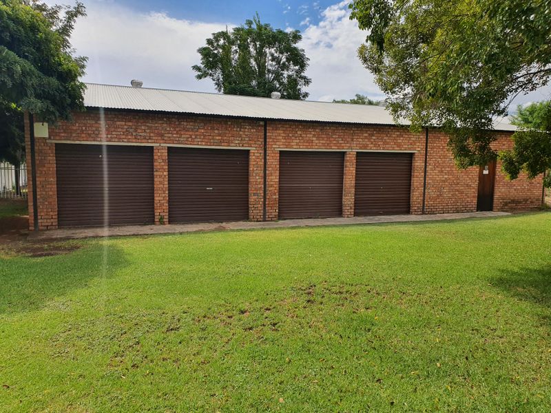 A detached four-car garage building featuring face brick construction, roller shutter doors, and a corrugated metal roof set within a grassy yard.