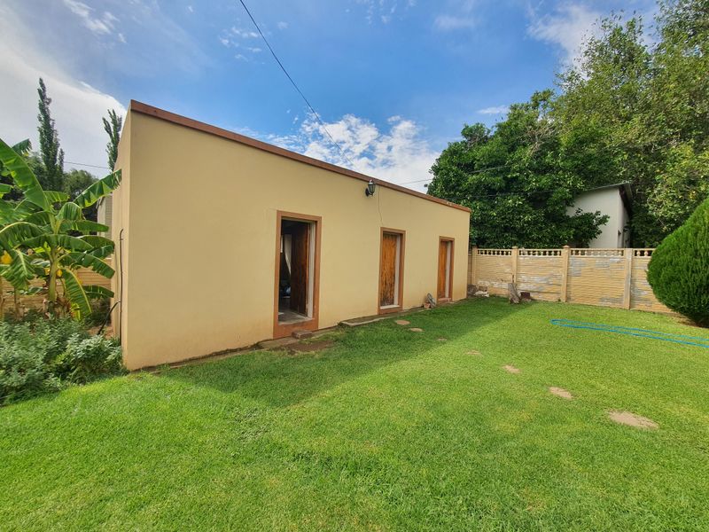 Rear view of the property featuring a lawn, garden area, and a solid boundary wall with visible exterior access points.