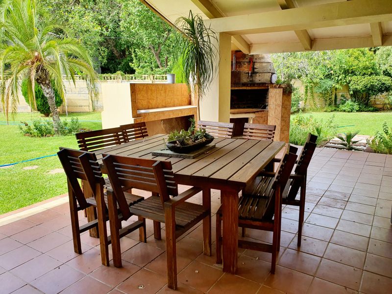 A covered outdoor patio featuring a built-in brick braai and tiled flooring, overlooking a spacious garden area.